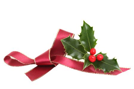 Red ribbon bow and a sprig of fresh holly with ripe berries isolated against whiteの写真素材