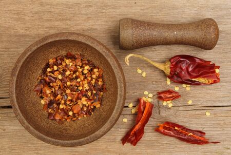 Pestle and mortar with dried red chilli peppers, flakes and seeds on an old weathered wooden boardの写真素材