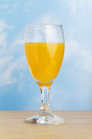 Fresh orange juice in a stem glass on a wooden surface against a blue skyの写真素材