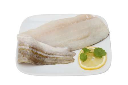 Fresh raw cod fillet with lemon and parsley garnish on a plate isolated against white