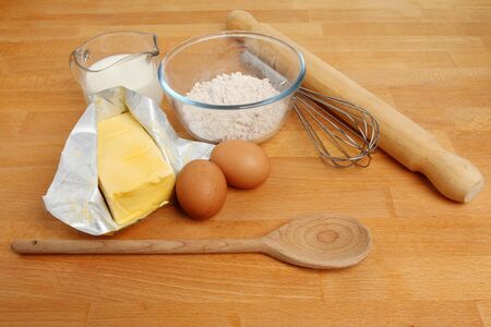 Baking ingredients, flour,eggs,milk and margarine with a whisk,wooden spoon and a rolling pin on a wooden worktopの写真素材