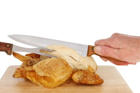 Hand holding a knife carving a whole cooked chicken on a wooden board against a white backgroundの写真素材