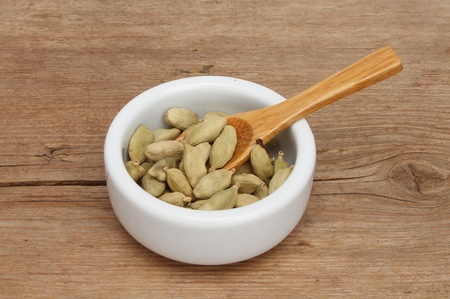 Whole cardamom seeds in a ramekin with a wooden spoon on a background of weathered woodの写真素材