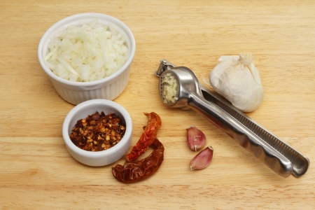 Chopped onions chilli, garlic and a garlic press on a wooden boardの写真素材
