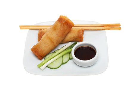 Pancake rolls, salad, soy sauce and chopsticks on a plate isolated against white