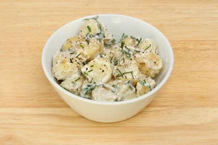 Potato salad in a bowl on a wooden boardの写真素材