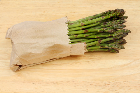Asparagus wrapped in brown paper on a wooden boardの写真素材