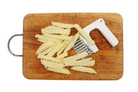 Crinkle cut raw potato chips with cutter on a wooden board isolated against whiteの写真素材