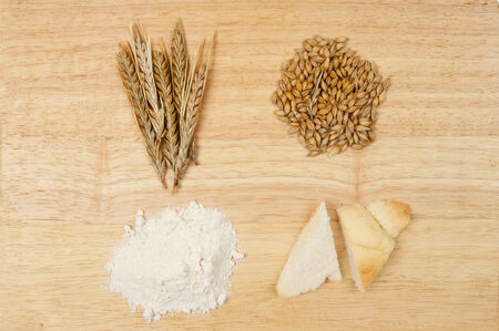 Wheat ears, wheat grains, flour and bread on a wooden boardの写真素材
