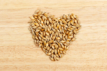 Wheat grains in the shape of a heart on a wooden boardの写真素材