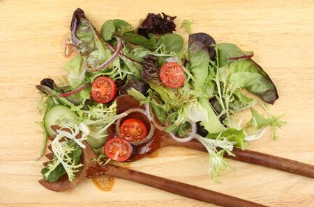 Salad with dressing and wooden salad servers on a wooden boardの写真素材