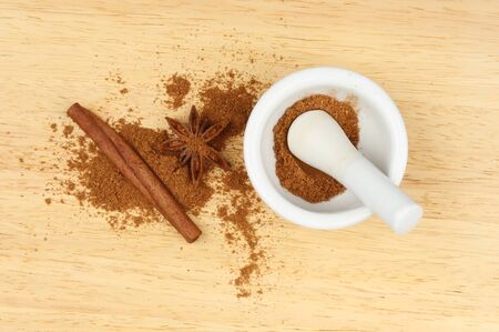 Chinese five spice in a pestle and mortar with star anise and cinnamon on a wooden boardの写真素材