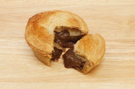 Freshly baked steak pie with a slice cut on a wooden boardの写真素材