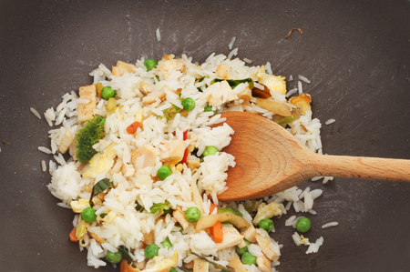 Closeup of chicken, egg and vegetable stir fried rice in a wok with a wooden spoonの写真素材