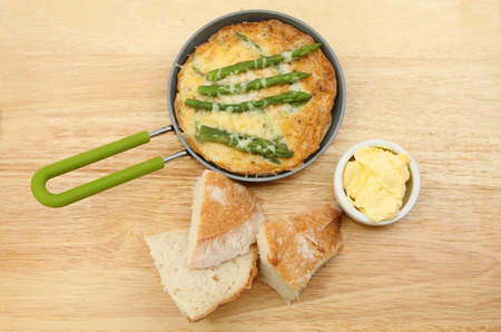 Individual asparagus and cheese Frittata with crusty bread and butter on a woodwn chopping boardの写真素材