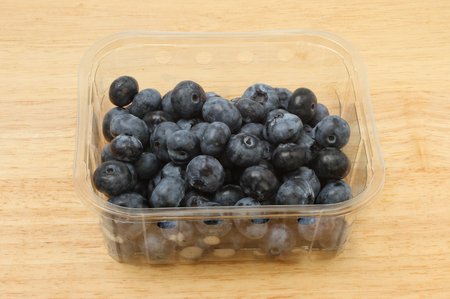 Fresh blueberries in a plastic punnet on a wooden boardの写真素材
