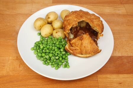 Steak pie new potatoes and peas on a plate on a wooden tabletopの写真素材