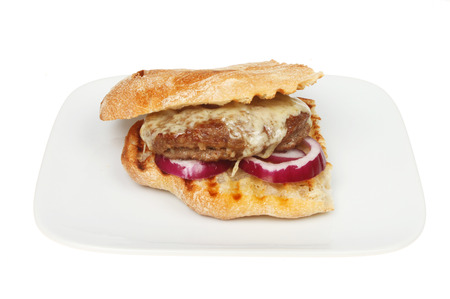 Cheeseburger with red onion in a ciabatta roll on a plate isolated against whiteの写真素材