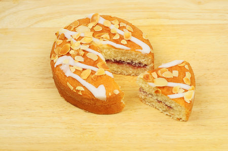 Cherry Bakewell cake with a slice cut out on a wooden chopping boardの写真素材