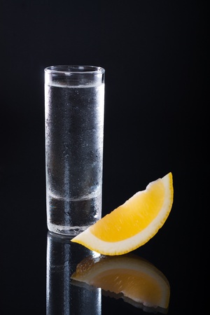 Shot glass filled with clear alcohol on a black backgroundの写真素材