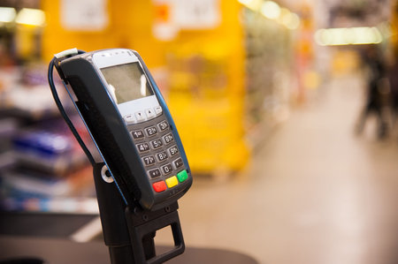 Empty cash desk with payment terminal and customers in queue in supermarket