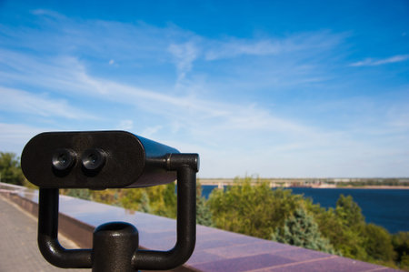 Observation binoculars against the blue sky and river.