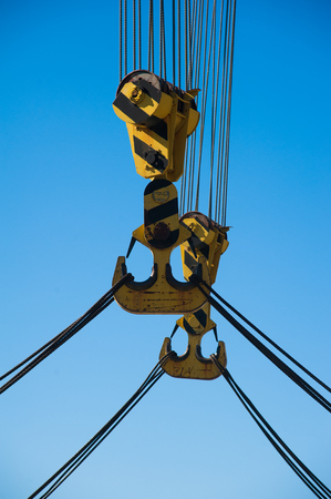 Loading in port. Floating port crane on blue sky background. Chains and hooks hoist with slings for loading in the port close-upの写真素材