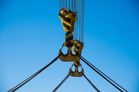 Loading in port. Floating port crane on blue sky background. Chains and hooks hoist with slings for loading in the port close-upの写真素材