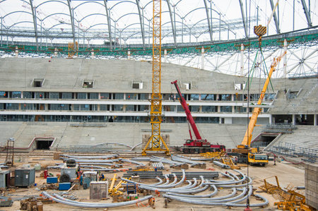 Stadium construction. Construction equipment and workers on the construction of a football stadium....