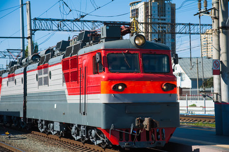 Red train locomotive on rail tracks and railway platform. Train and railway station.