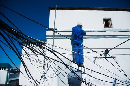 An electrician works among the many wires on the roof of a high-rise buildingの写真素材