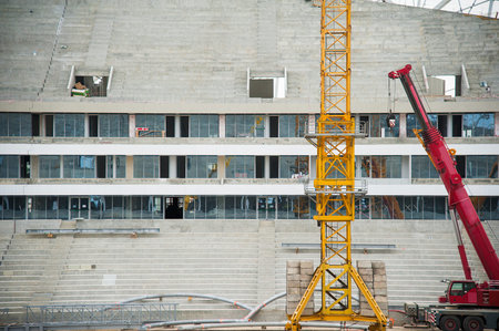 Stadium construction. Construction equipment and workers on the construction of a football stadium....