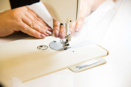 Woman hands with fabric at sewing machine. Seamstress working behind her equipment. Tailoring process, designer workshop, garment industry conceptの写真素材