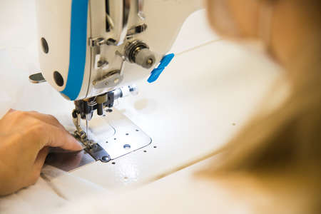 Woman hands with fabric at sewing machine. Seamstress working behind her equipment. Tailoring process, designer workshop, garment industry conceptの写真素材