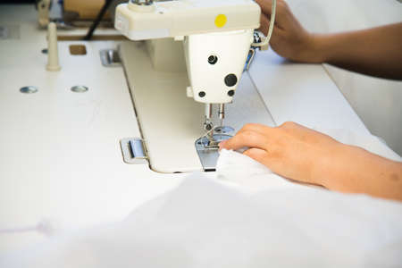 Woman hands with fabric at sewing machine. Seamstress working behind her equipment. Tailoring process, designer workshop, garment industry conceptの写真素材