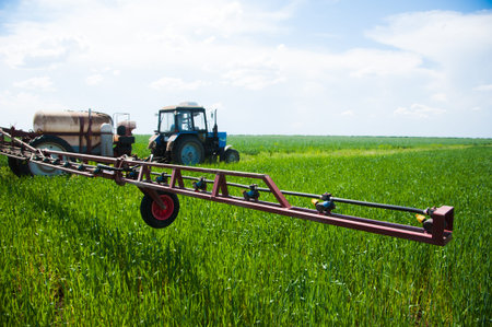 Tractor spraying pesticides wheat field with sprayer at spring