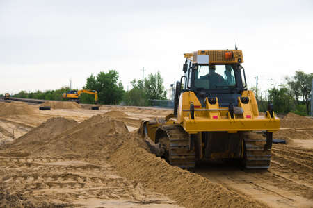Repair of the old and construction of a new asphalt road. The excavators, graders and road rollers working on the new road construction site.の写真素材