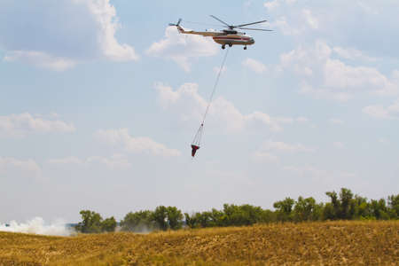 Firefighting helicopter with fire bucket flies against a clear blue skyの写真素材