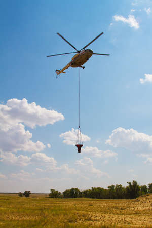 Firefighting helicopter with fire bucket flies against a clear blue skyの写真素材