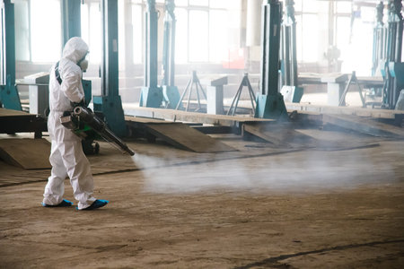 Worker in a protective suit handles industrial premises, buildings, and interiors to protect against...