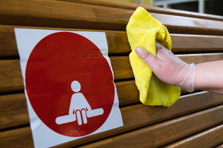 Woman wearing a glove wipes the surface of the seat back in a public place with a disinfectant. Safety during the COVID-19 pandemic. There is a sticker on the seat with a distance symbolの写真素材