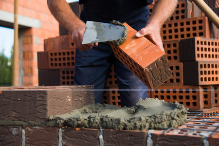 Bricklayer worker installing brick masonry on exterior wall. Professional construction worker laying bricks.の写真素材