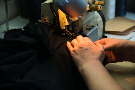 Woman hands with fabric at sewing machine. Seamstress working behind her equipment. Tailoring process, designer workshop, garment industry conceptの写真素材