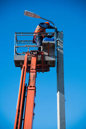 Worker with helmet and safety protective equipment installs new diode lights. Worker in lift bucket repair light pole. Modernization of street lamps.の写真素材