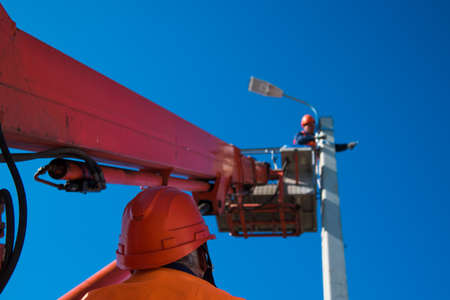 Worker with helmet and safety protective equipment installs new diode lights. Worker in lift bucket repair light pole. Modernization of street lamps.の写真素材