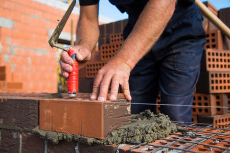 Bricklayer worker installing brick masonry on exterior wall. Professional construction worker laying bricks.の写真素材