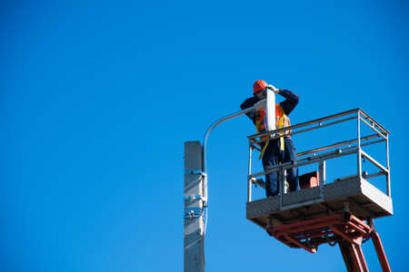 Worker with helmet and safety protective equipment installs new diode lights. Worker in lift bucket repair light pole. Modernization of street lamps.の写真素材