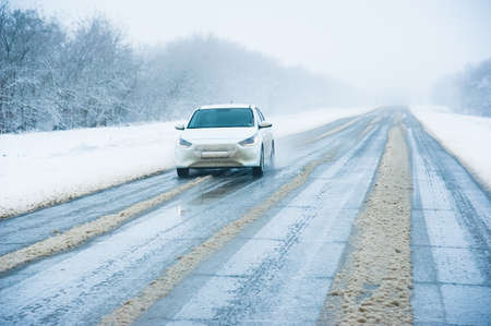 Lonely car driving on a winter road in a snowfall. Snow-covered highway on a winter day. Difficult road conditions for road transportの写真素材