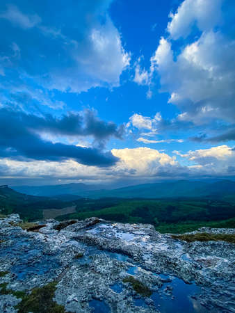 Dramatic vertical panoramic landscape view of the mountains, river and cloudy sky with sun flare in the skyの写真素材