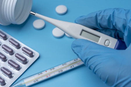A gloved hand holds an electronic thermometer on a blue background.の写真素材